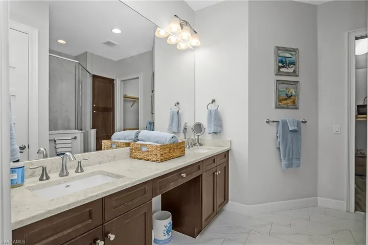 Owner's bathroom with double vanity, a stall shower, light marble finish flooring, and a spacious closet