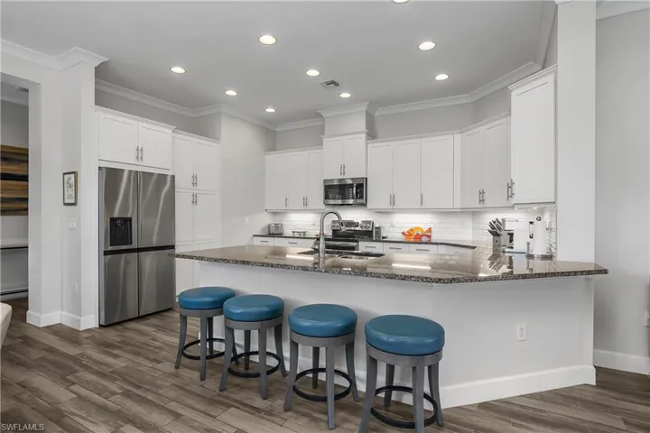 Kitchen with a peninsula, stainless steel appliances, dark stone counters, white cabinetry, and recessed lighting.