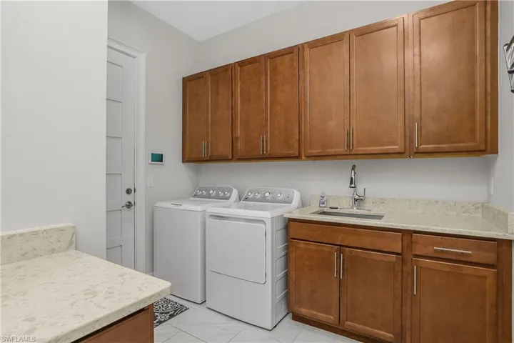 Large Laundry area with washer and dryer, sink, cabinet space, and light marble finish flooring.