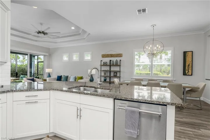Kitchen with dishwasher, white cabinets, open floor plan, stone countertops, and ornamental molding