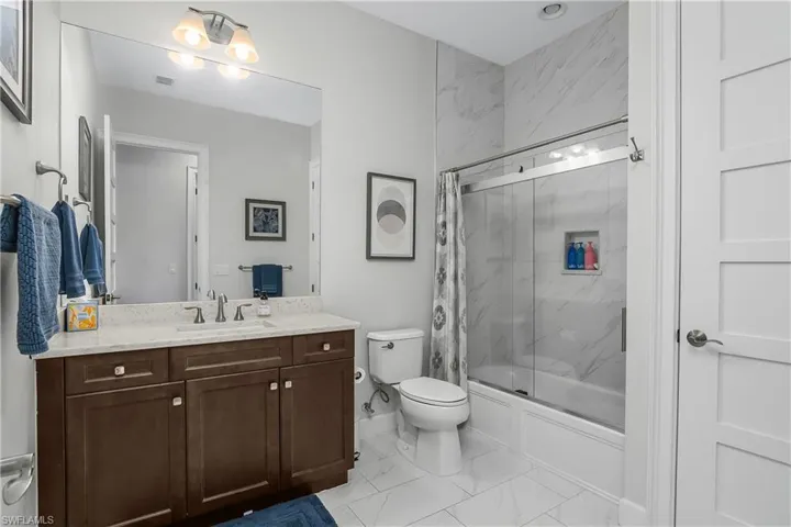 Guest Bathroom with vanity, enclosed tub / shower combo, and light marble finish flooring
