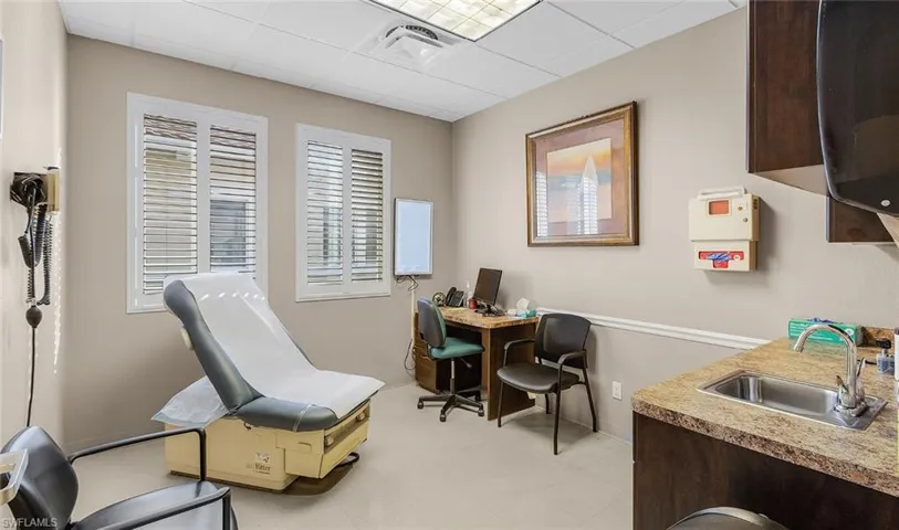 Office space with a paneled ceiling, light floors, visible vents, and a sink