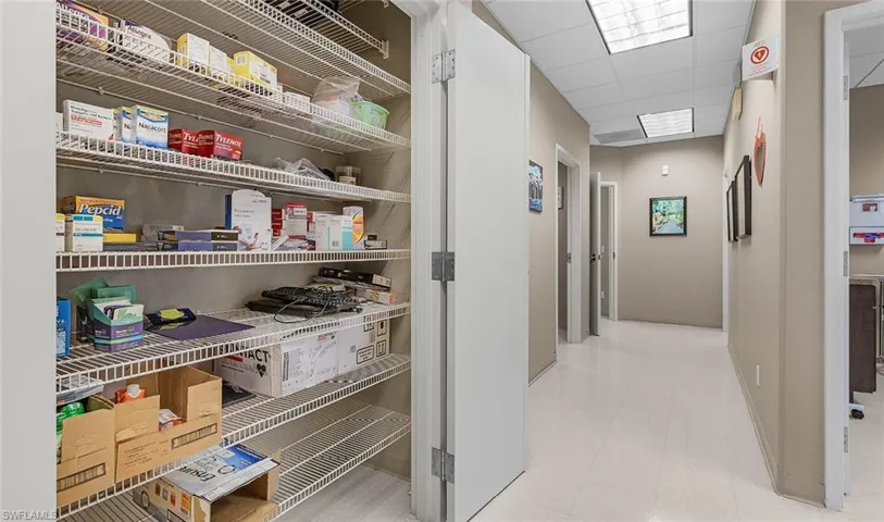 Hallway featuring baseboards, a drop ceiling, and light floors