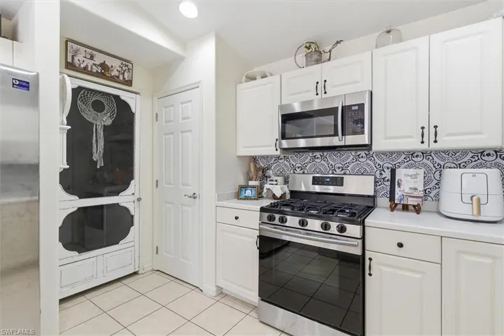 Kitchen with appliances with stainless steel finishes, light countertops, white cabinetry, decorative backsplash, and light tile patterned floors