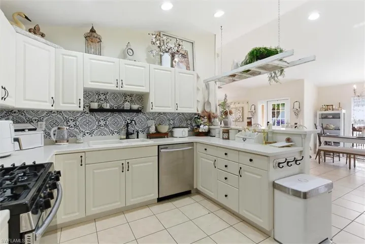 Kitchen with a peninsula, appliances with stainless steel finishes, light tile patterned flooring, decorative backsplash, and white cabinetry