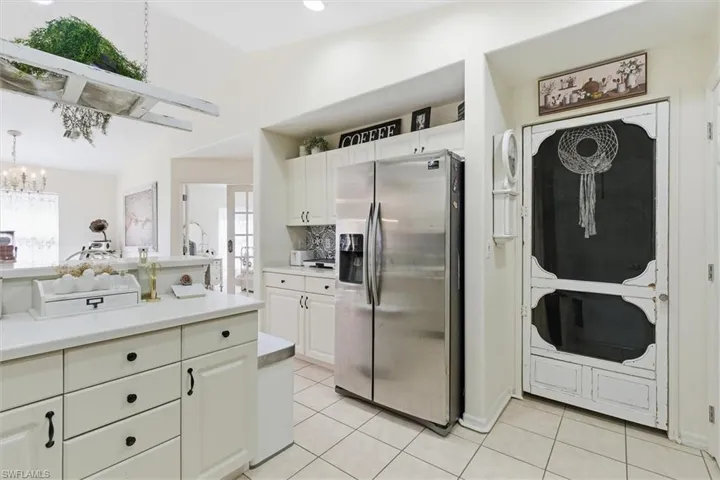 Kitchen with stainless steel fridge, white cabinetry, vaulted ceiling, decorative backsplash, and light tile patterned floors