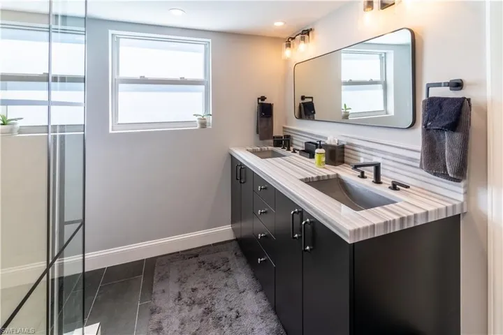 Full bathroom with double vanity, dark tile patterned floors, and a shower with shower door