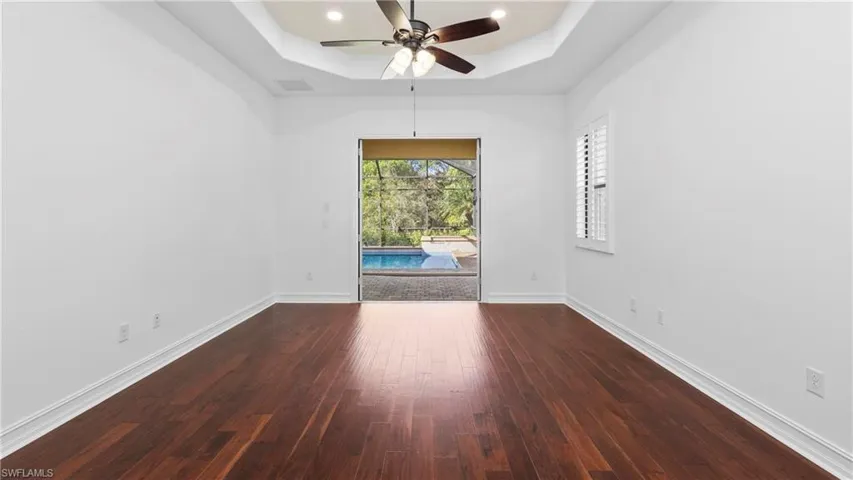 Spare room featuring ceiling fan, a raised ceiling, dark wood-style floors, a sunroom, and recessed lighting