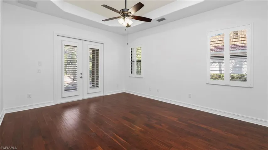 Spare room featuring a raised ceiling, dark wood-style flooring, french doors, a ceiling fan, and plenty of natural light