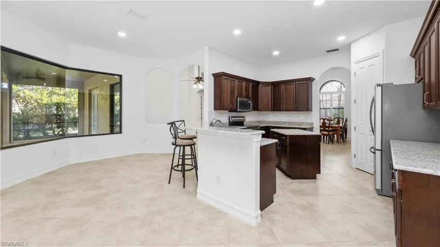 Kitchen with arched walkways, dark wood finish cabinets, a center island, light stone counters, and a breakfast bar area