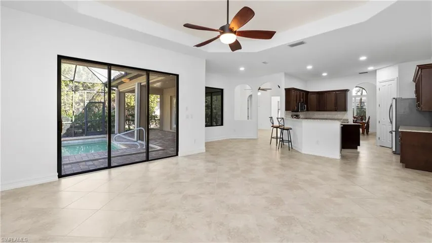 Unfurnished living room featuring a ceiling fan, arched walkways, a raised ceiling, a sunroom, and recessed lighting