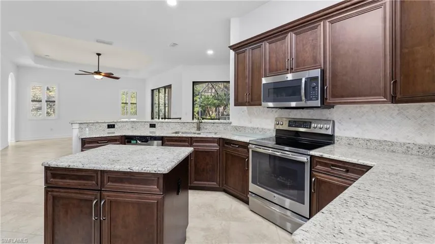 Kitchen featuring a raised ceiling, stainless steel appliances, dark wood finish cabinetry, light stone counters, and a peninsula