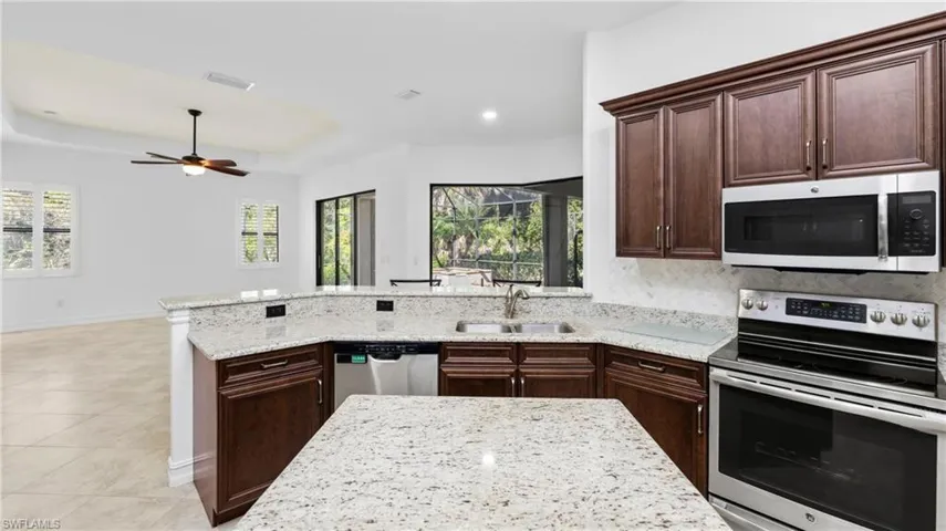 Kitchen with dark wood finish cabinets, stainless steel appliances, a peninsula, light stone countertops, and a raised ceiling