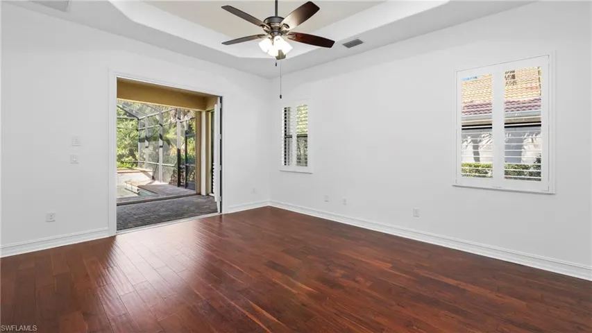 Unfurnished room featuring a raised ceiling, dark wood-style flooring, and ceiling fan