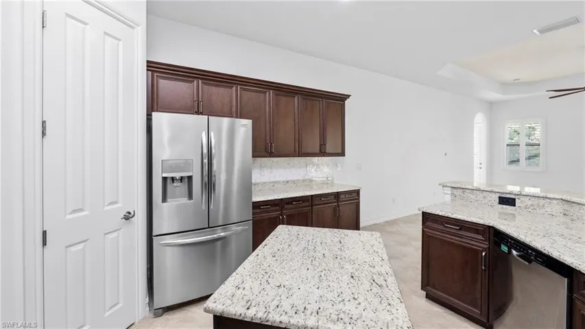 Kitchen with stainless steel appliances, light stone countertops, dark wood finish cabinetry, and a kitchen island