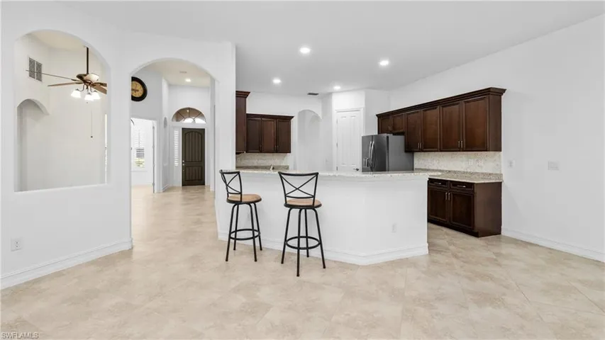 Kitchen featuring dark wood finish cabinetry, backsplash, ceiling fan, and arched walkways