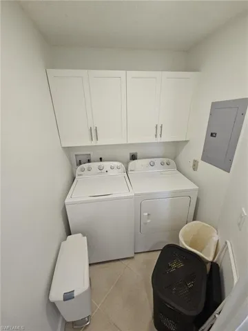 Laundry area with electric panel, washing machine and clothes dryer, cabinet space, and light tile patterned floors