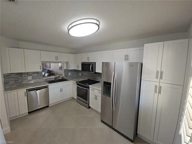 Kitchen featuring stainless steel appliances, white cabinets, backsplash, a textured ceiling, and light tile patterned floors