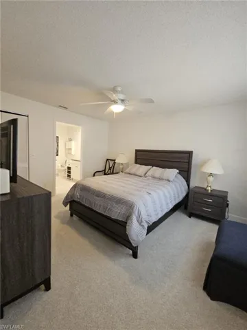 Bedroom with light carpet, a textured ceiling, ensuite bath, and a ceiling fan