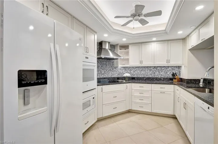 Kitchen featuring a tray ceiling, white appliances, and backsplash
