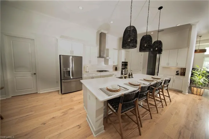 Kitchen featuring light wood-type flooring, a breakfast bar area, an island with sink, wall chimney exhaust hood, and appliances with stainless steel finishes