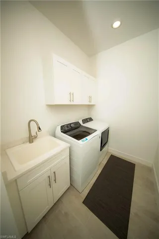 Washroom with washing machine and dryer, cabinets, sink, and light tile patterned floors