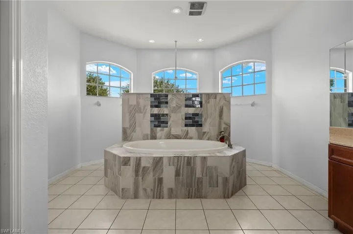 Bathroom with a relaxing tiled tub, vanity, and tile patterned floors