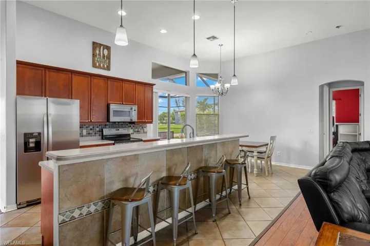 Kitchen featuring a breakfast bar area, light tile patterned floors, appliances with stainless steel finishes, decorative backsplash, and decorative light fixtures