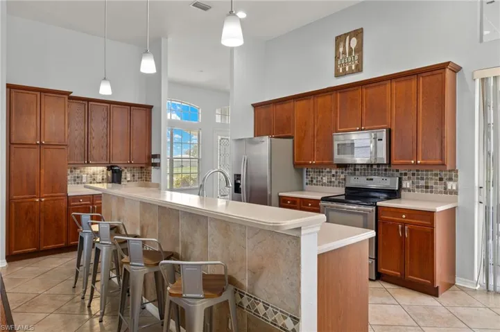Kitchen featuring light tile patterned flooring, tasteful backsplash, pendant lighting, appliances with stainless steel finishes, and a kitchen breakfast bar
