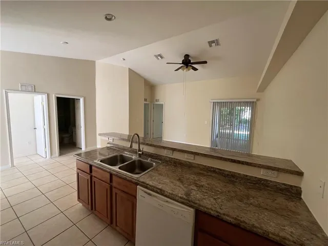 Kitchen with dishwasher, light tile patterned floors, lofted ceiling, brown cabinetry, and ceiling fan