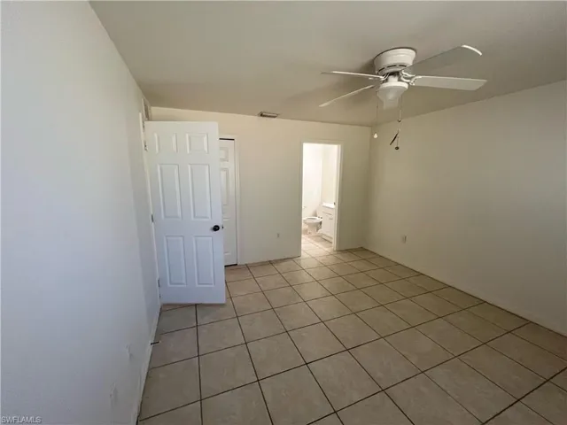 Unfurnished bedroom with ceiling fan, light tile patterned flooring, and ensuite bathroom