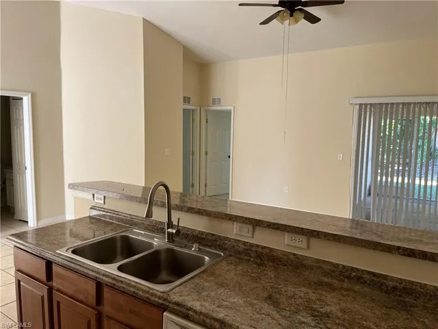 Kitchen with dark countertops, ceiling fan, light tile patterned floors, and brown cabinets