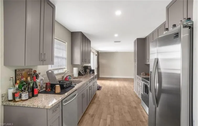 Kitchen featuring gray cabinets, appliances with stainless steel finishes, light stone counters, light wood finished floors, and recessed lighting