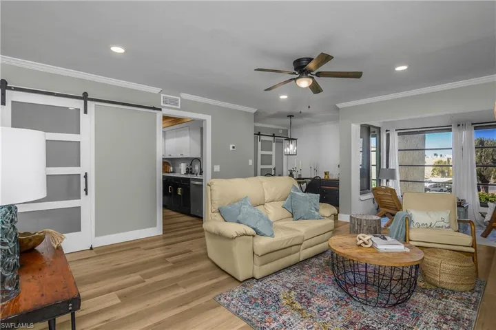 Living area with a barn door, recessed lighting, a ceiling fan, light wood-style flooring, and crown molding