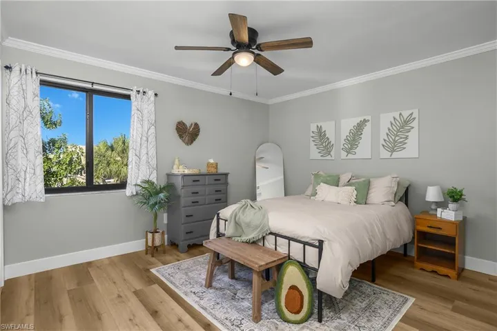 Bedroom with crown molding, luxry vinyl wide plank flooring, and a ceiling fan.
