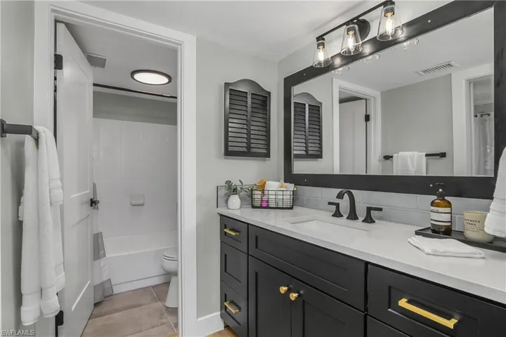 Bathroom featuring new vanity, quartz countertop shower / bath combination with curtain, and light tile patterned flooring