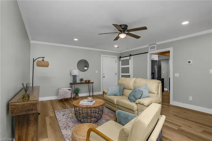 Living room with a barn door, ceiling fan, light wood-type flooring, recessed lighting, and ornamental molding