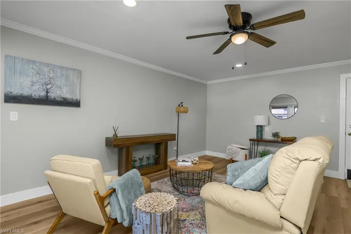 Living room featuring wood finished floors, crown molding, craftsman 6 inch base molding, ceiling fan.