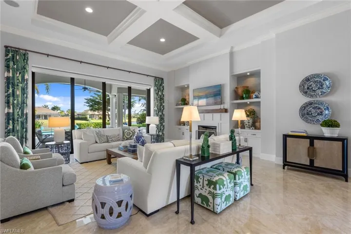 Living room featuring coffered ceiling, built in shelves, ornamental molding, a glass covered fireplace, and beamed ceiling