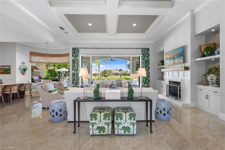 Living room with coffered ceiling, beamed ceiling, a fireplace with raised hearth, built in features, and ornamental molding