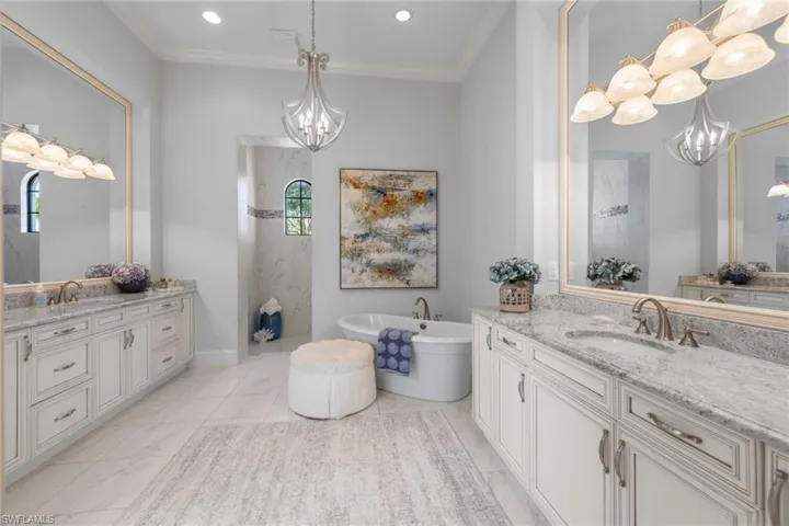 Full bathroom featuring a chandelier, two vanities, a soaking tub, ornamental molding, and a marble finish shower
