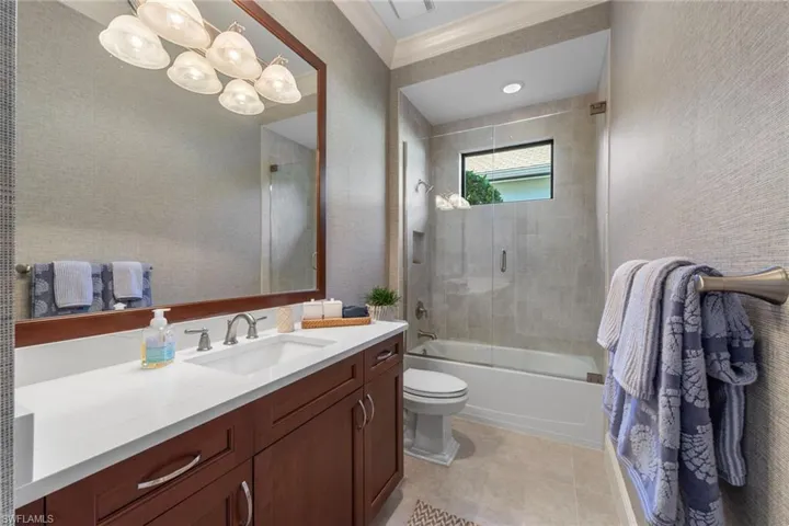 Full bathroom featuring vanity, combined bath / shower with glass door, ornamental molding, light tile patterned flooring, and a textured wall