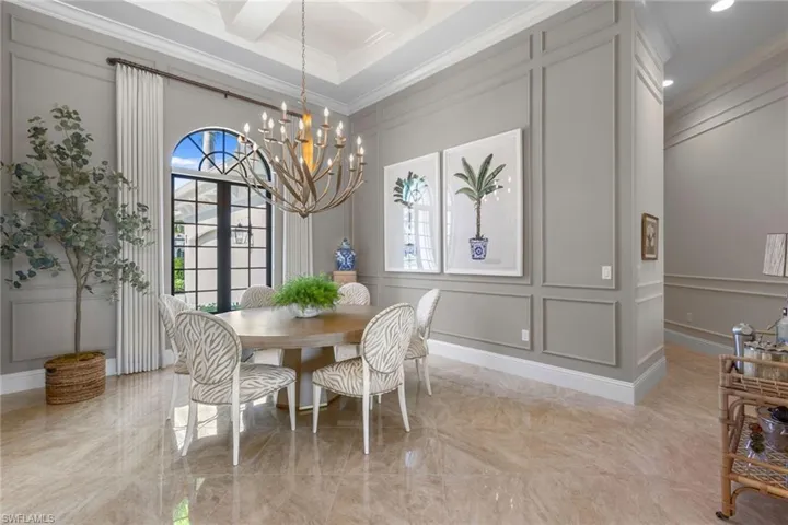Dining room featuring a decorative wall, light marble finish floors, crown molding, plenty of natural light, and coffered ceiling