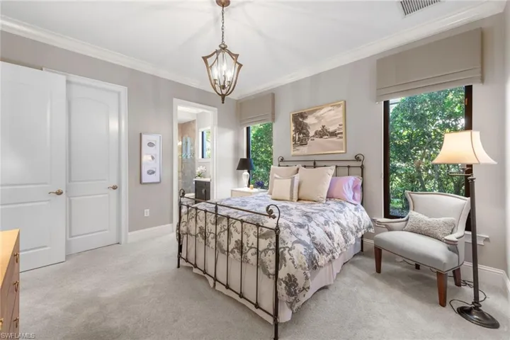 Bedroom with multiple windows, crown molding, carpet, ensuite bath, and a chandelier