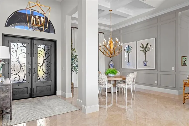Foyer entrance featuring a chandelier, a decorative wall, light marble finish floors, coffered ceiling, and ornamental molding