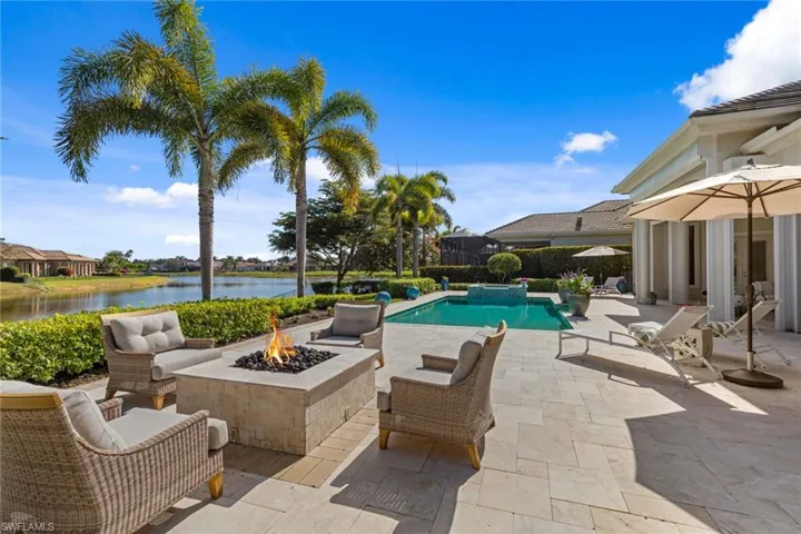 View of pool featuring a patio, a pool with connected hot tub, a water view, and an outdoor living space with a fire pit