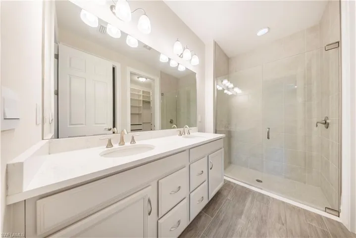 Bathroom with double vanity, a stall shower, a walk in closet, and wood tiled floors