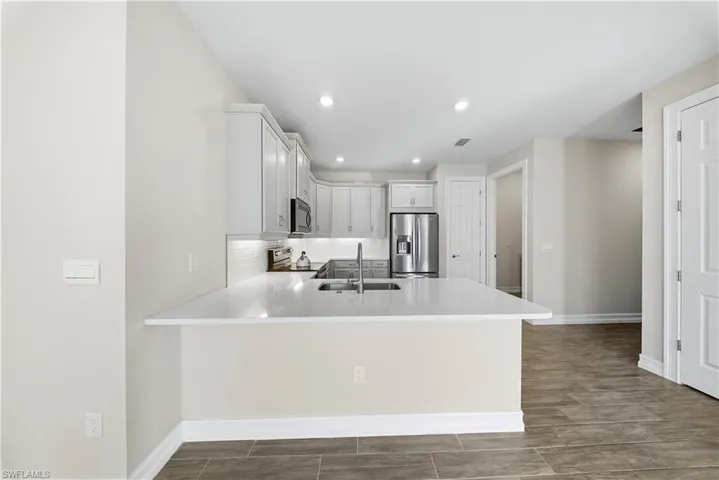 Kitchen featuring white cabinets, stainless steel appliances, a peninsula, wood tiled floors, and light stone countertops