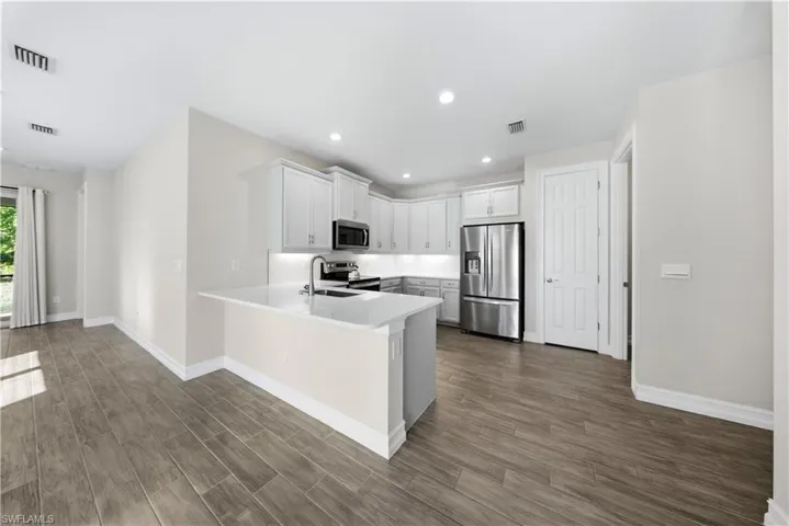 Kitchen with stainless steel appliances, white cabinetry, wood tiled floors, a peninsula, and recessed lighting