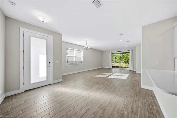 Empty room with a chandelier, wood finish floors, and healthy amount of natural light